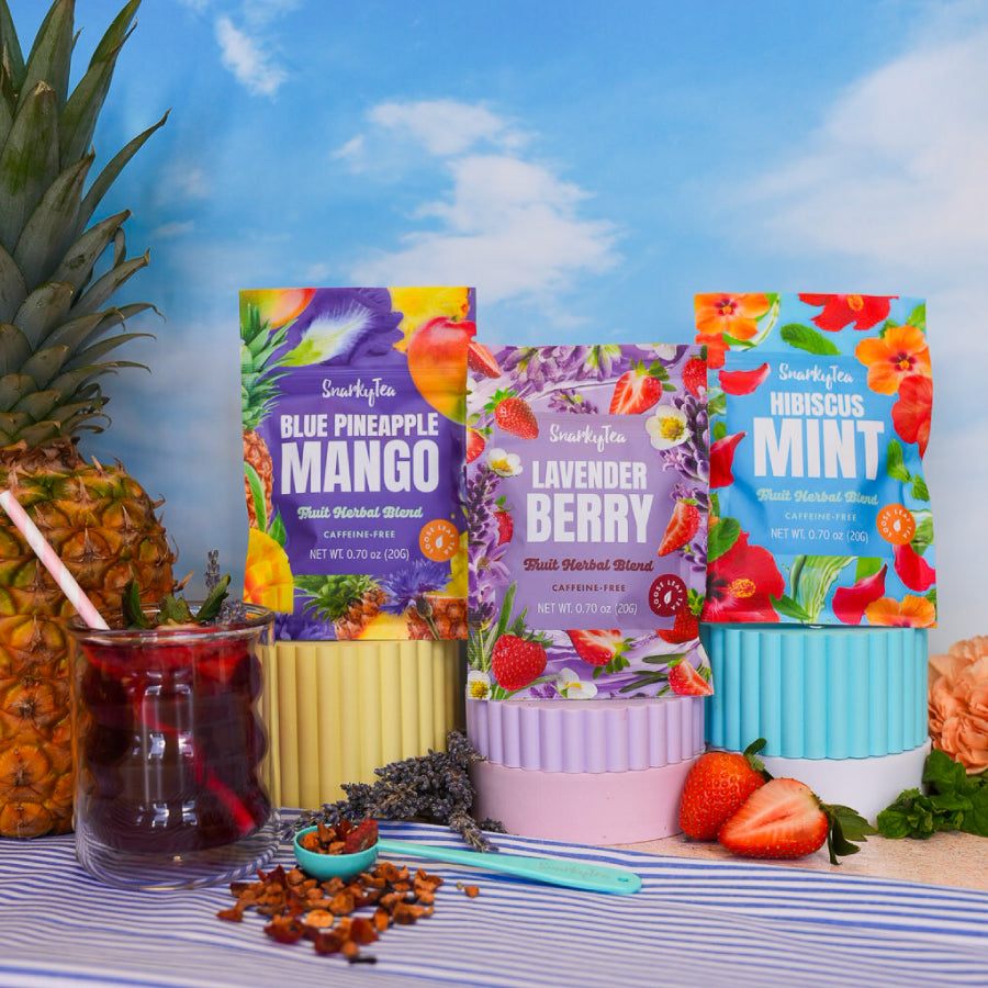 Three packages of Snarky Tea Fruit Herbal Blends with colorful designs on a white background. Blue Pineapple Mango, Hibiscus Mint, Lavender Berry.